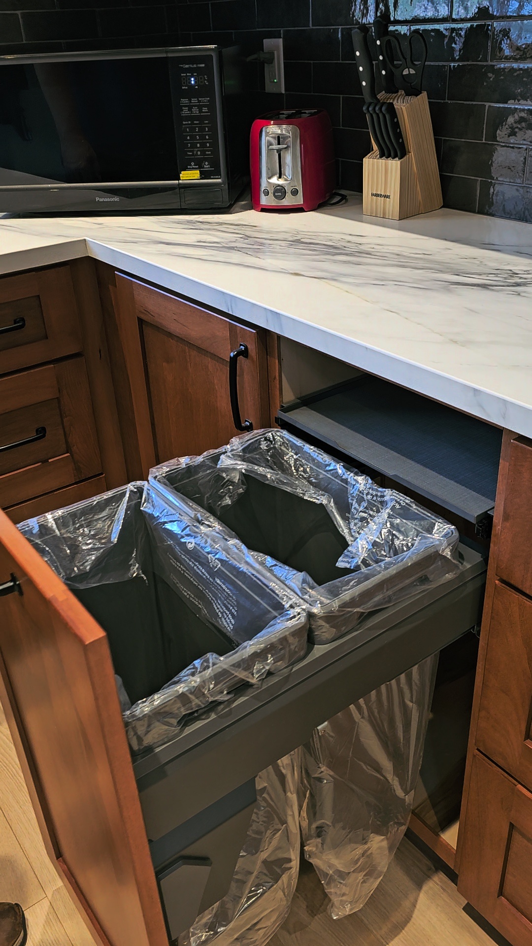 A soft-close garbage pull-out system is a kitchen storage solution that hides waste and recycling bins inside a cabinet, typically sliding out on tracks for easy access. These systems help save floor space, improve kitchen hygiene, and keep trash out of sight from guests and pets. Cedar Lane Custom Kitchens